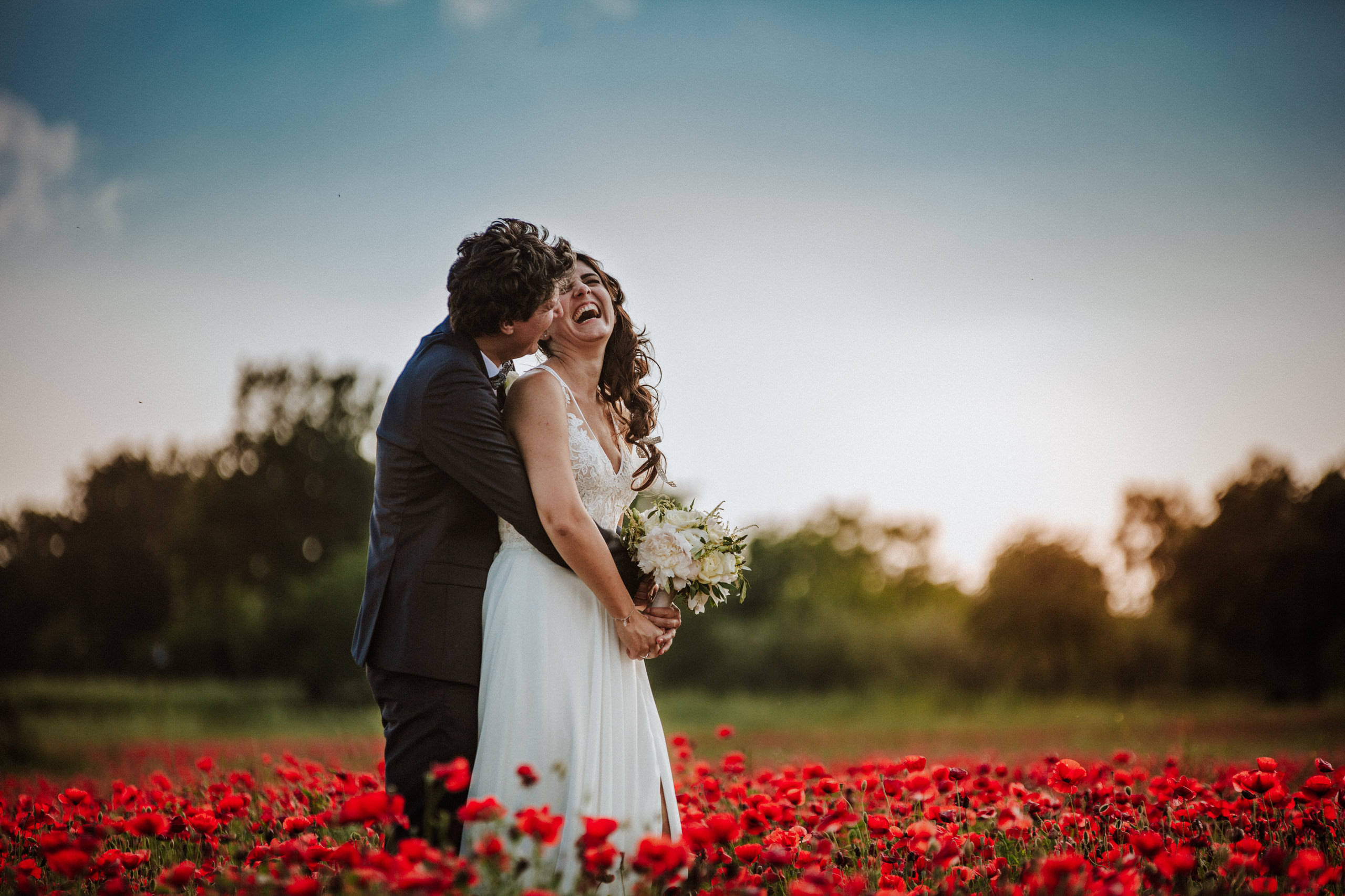 momento naturale di sposi che ridono in un campo di papaveri al tramonto